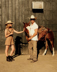 Two people in cowboy hats standing next to a horse in front of a wooden building.