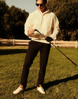 Luxury Western Golf apparel Man in a white shirt and sunglasses holding a golf club on a grassy field with trees in the background.
