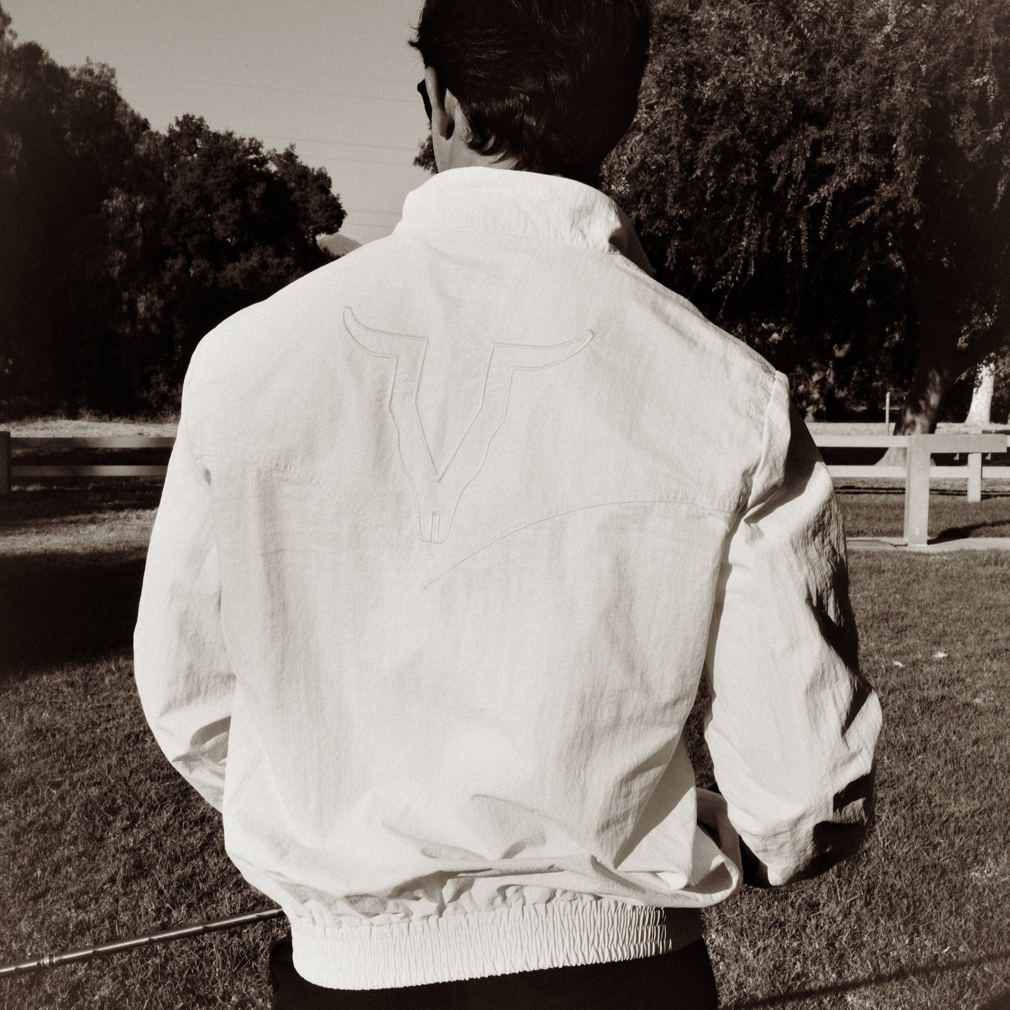 Luxury Western Golf apparel Person wearing a white jacket standing outdoors with trees and a fence in the background