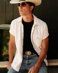 Luxury Western Golf apparel Man wearing a white cowboy hat, sunglasses, and a white shirt over a black t-shirt with blue jeans.