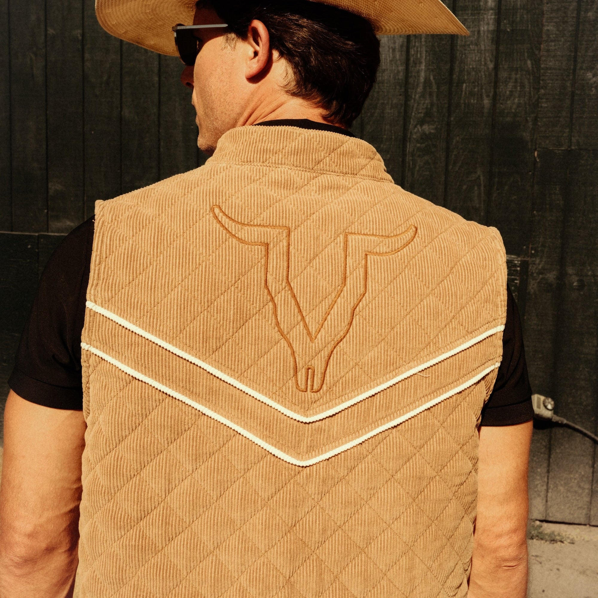 Luxury Western Golf apparel Person wearing a tan quilted vest with a bull emblem and a cowboy hat against a dark background